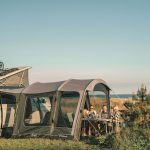 An image of a campervan in a coastal location. It has an awning attached and a table and chairs outside of it