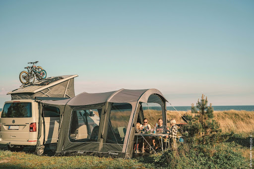 An image of a campervan in a coastal location. It has an awning attached and a table and chairs outside of it