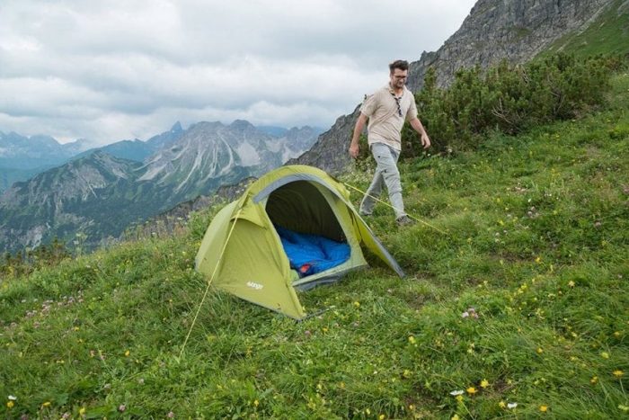 Man walking next to single person tent on a hill