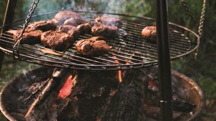 Burgers on camping grill over open fire.
