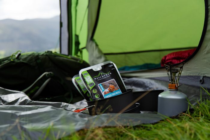 Tent set up with a gas stove and packets of food in a pan.