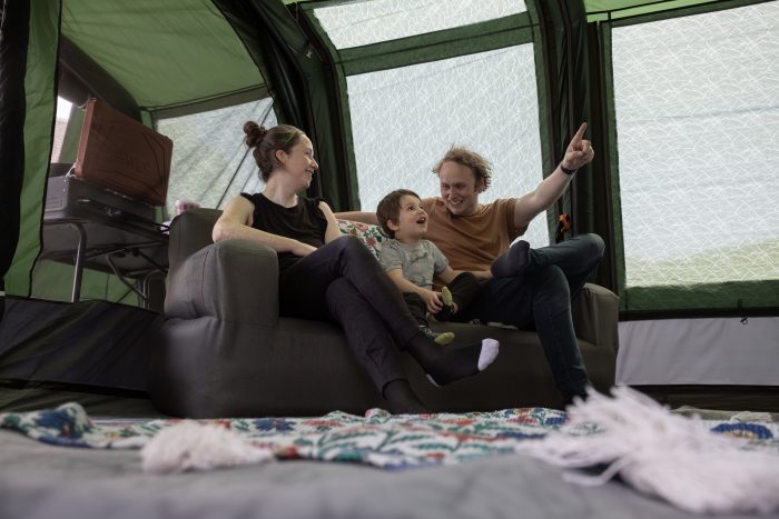 A family of four sits together on a couch inside a cosy tent, smiling and enjoying their time together.