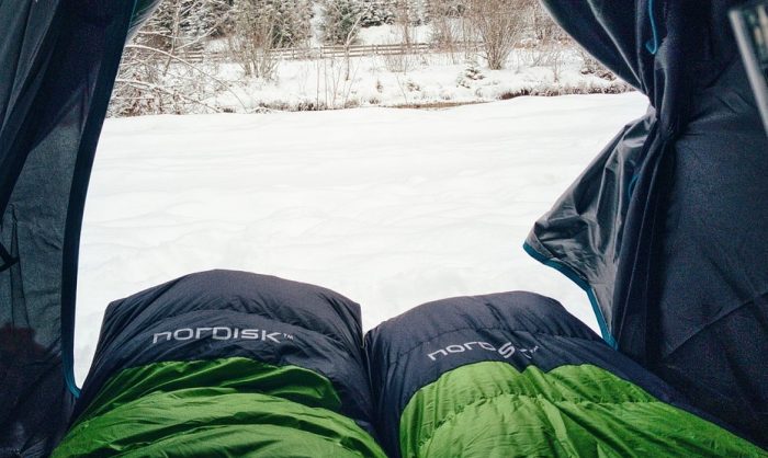 A person relaxes in a tent, their feet resting in the soft snow outside, enjoying the winter scenery.