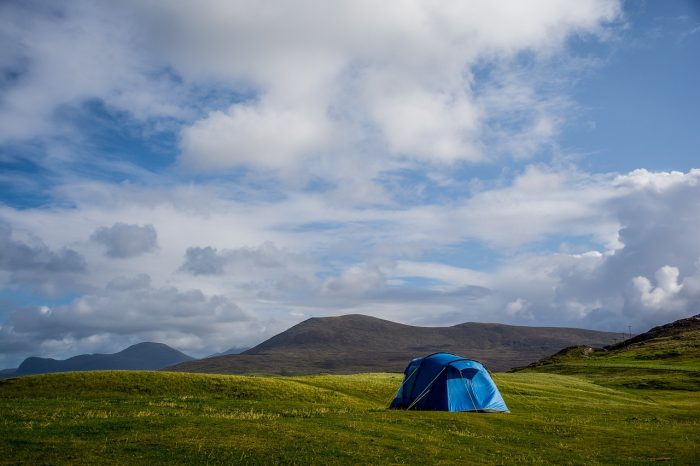 A blue tent perched on a grassy hill, surrounded by a serene landscape under a clear sky