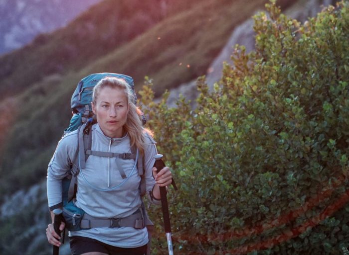 A woman with a backpack treks through the mountains, taking in the breathtaking views of the natural surroundings.