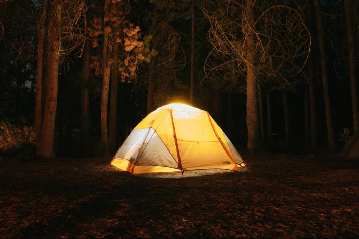 A tent in the woods that is lit up from the outside.