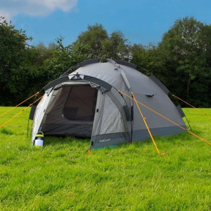 A tent set in a green field under a clear blue sky, surrounded by open space and natural scenery
